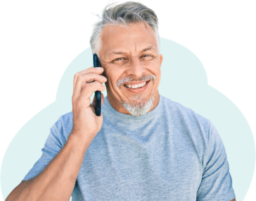 Un hombre con pelo gris sobre la frente sonríe mientras habla por teléfono. Lleva una camisa de algodón celeste y parece feliz con la conversación.
