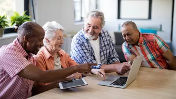 Grupo de 4 personas mayores sonriendo mientras miran una PC y una tableta