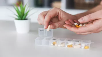 Primer plano de las manos de una mujer caucásica agregando pastillas al pastillero