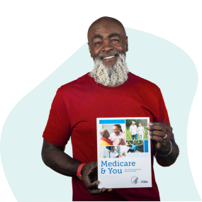Un hombre afroamericano con barba 60 con una blusa roja sosteniendo el manual Medicare y usted