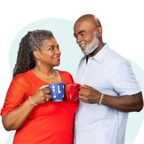 Una pareja afroamericana mirándose amorosamente y tintineando tazas. La mujer lleva una camisa roja y sostiene una taza azul, el hombre lleva una camisa celeste y sostiene una taza roja.