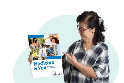 Mujer que sostiene el manual Medicare y usted en una mano y señala hacia él con la otra.