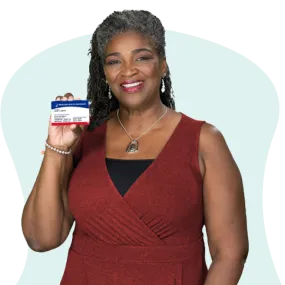 Mujer afroamericana con vestido rojo oscuro que sostiene su tarjeta de Medicare y sonríe.