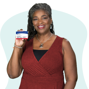 Mujer afroamericana con vestido rojo oscuro que sostiene su tarjeta de Medicare y sonríe.